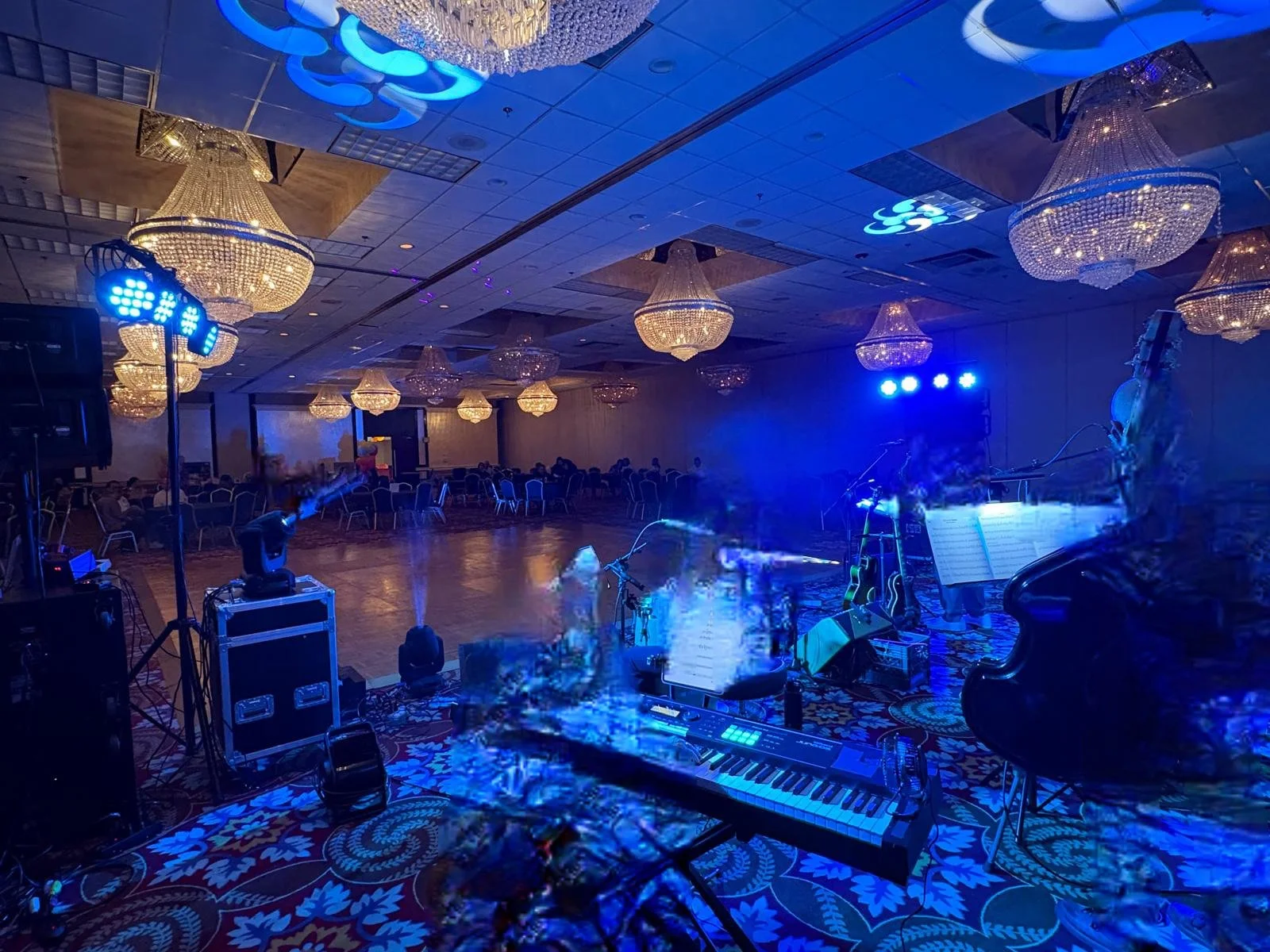 Empty ballroom with chandeliers, a stage with musical instruments, and blue stage lighting.