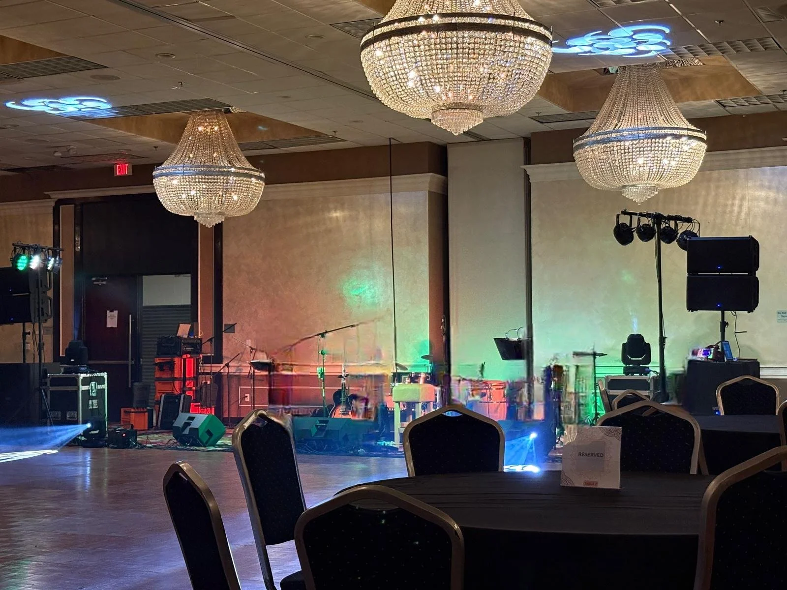 Empty banquet hall with chandeliers, a stage set for a performance with lighting, musical instruments, and sound equipment, and tables with reserved signs.