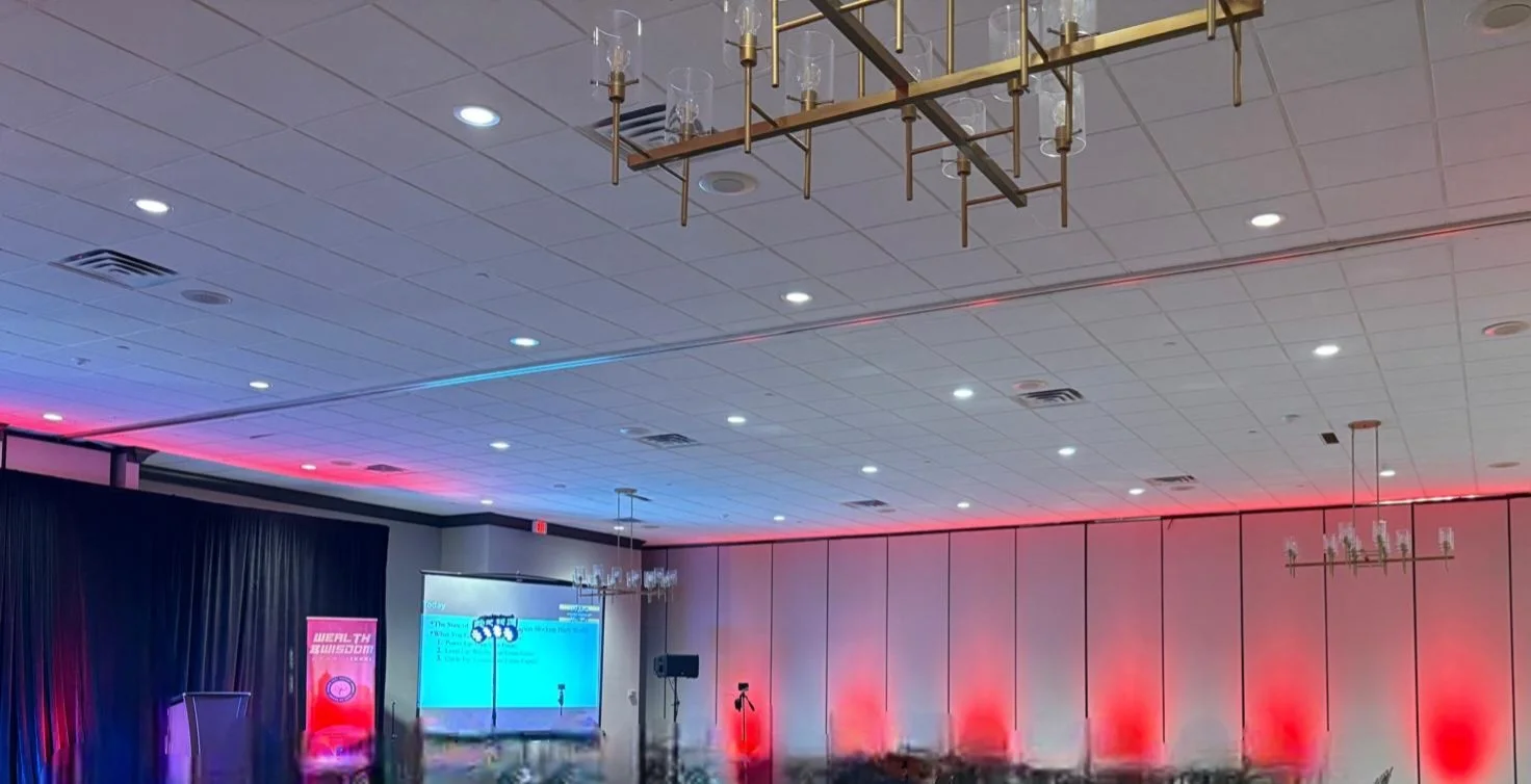 A decorated conference room with chandeliers, LED lighting accents, a podium, and a large presentation screen.