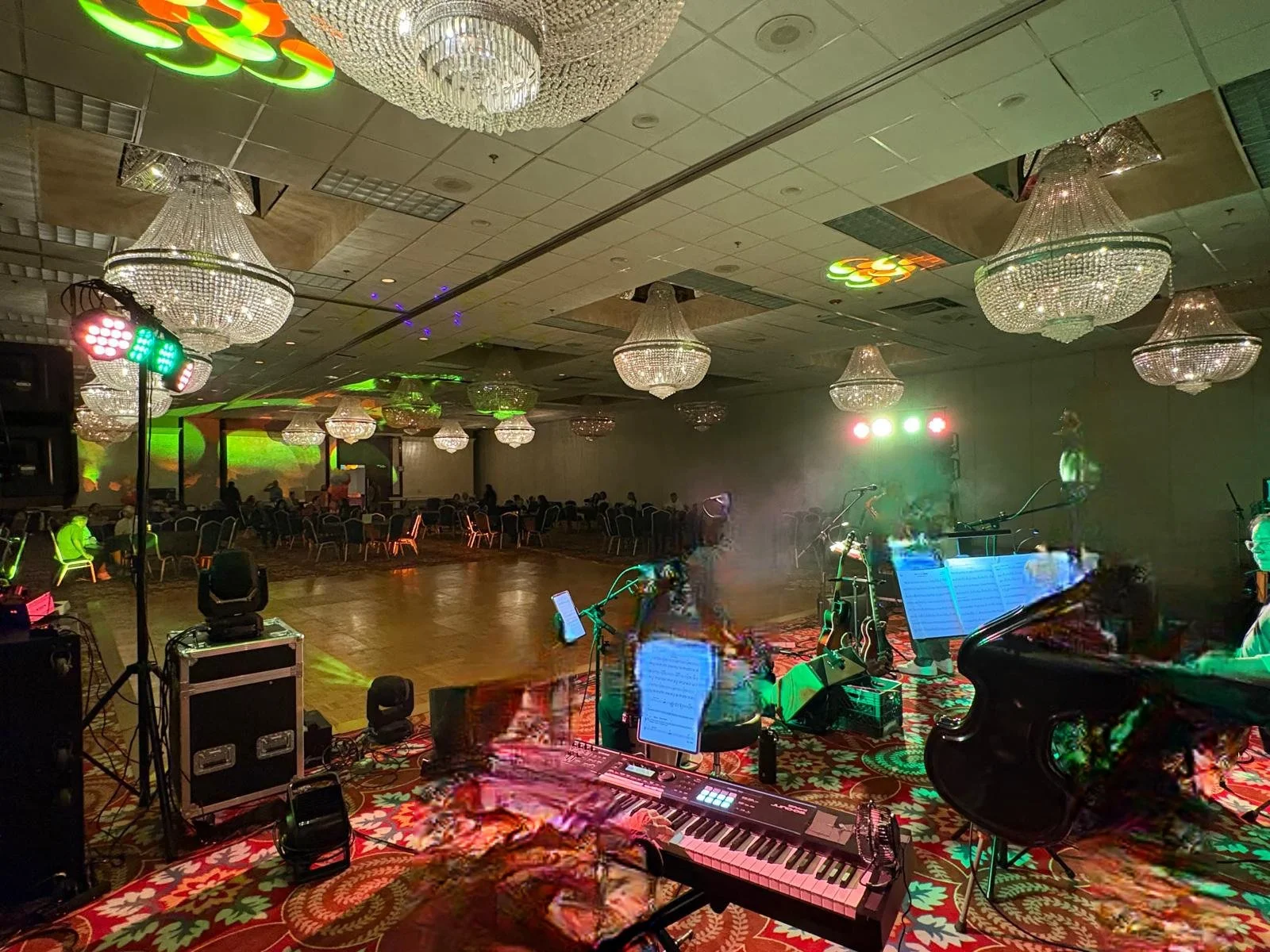 Empty banquet hall with chandeliers, stage with musical instruments, sheet music, lighting equipment, and a dance floor.