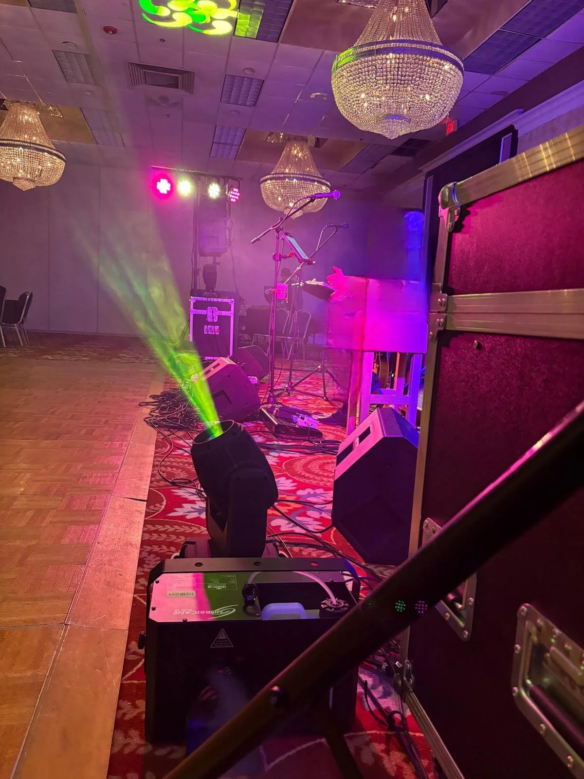Empty stage with musical equipment, colorful lights, chandeliers, and a red carpet in a banquet hall.