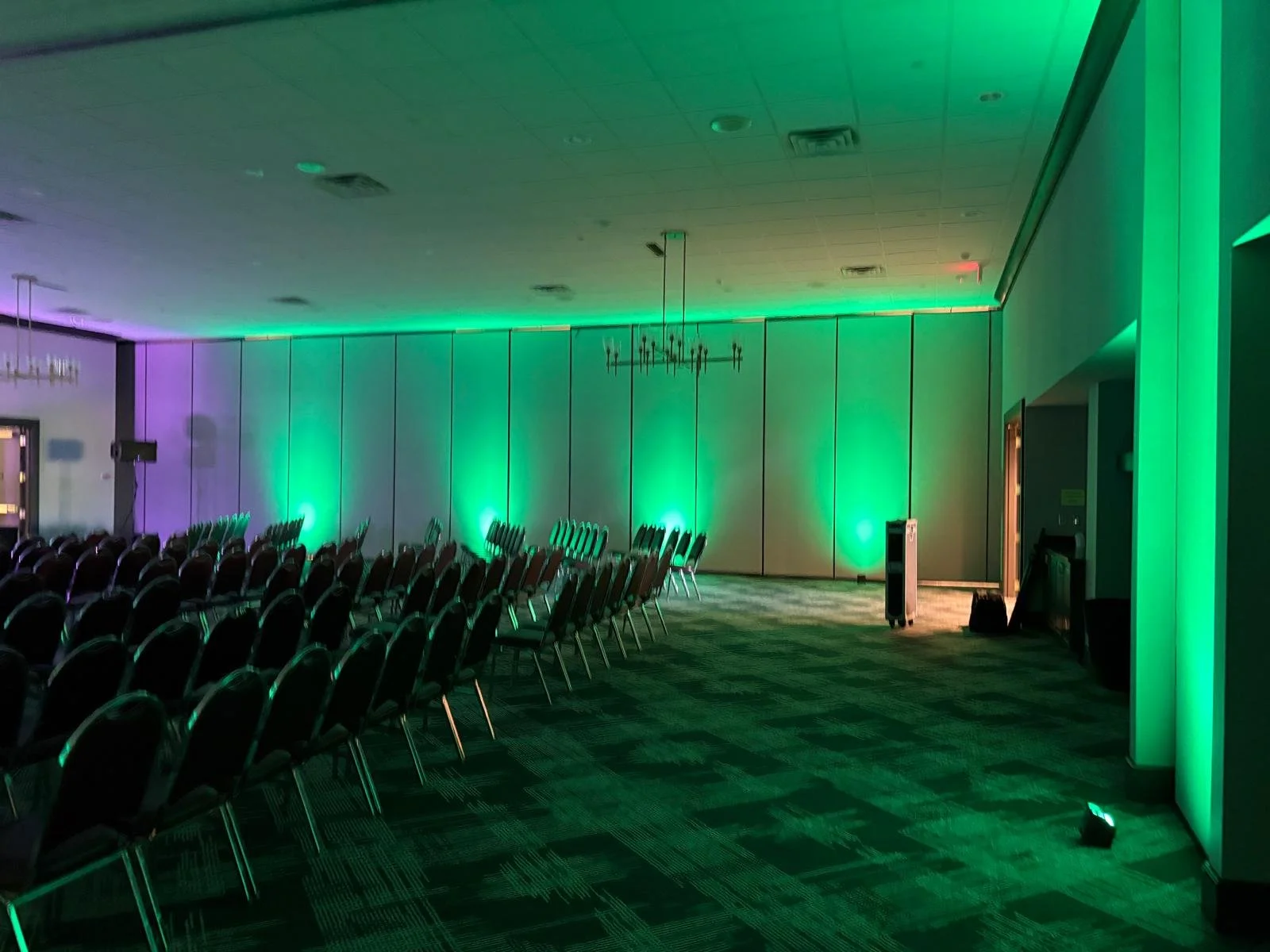 Empty conference room with rows of chairs facing a stage, illuminated with green and purple lighting.