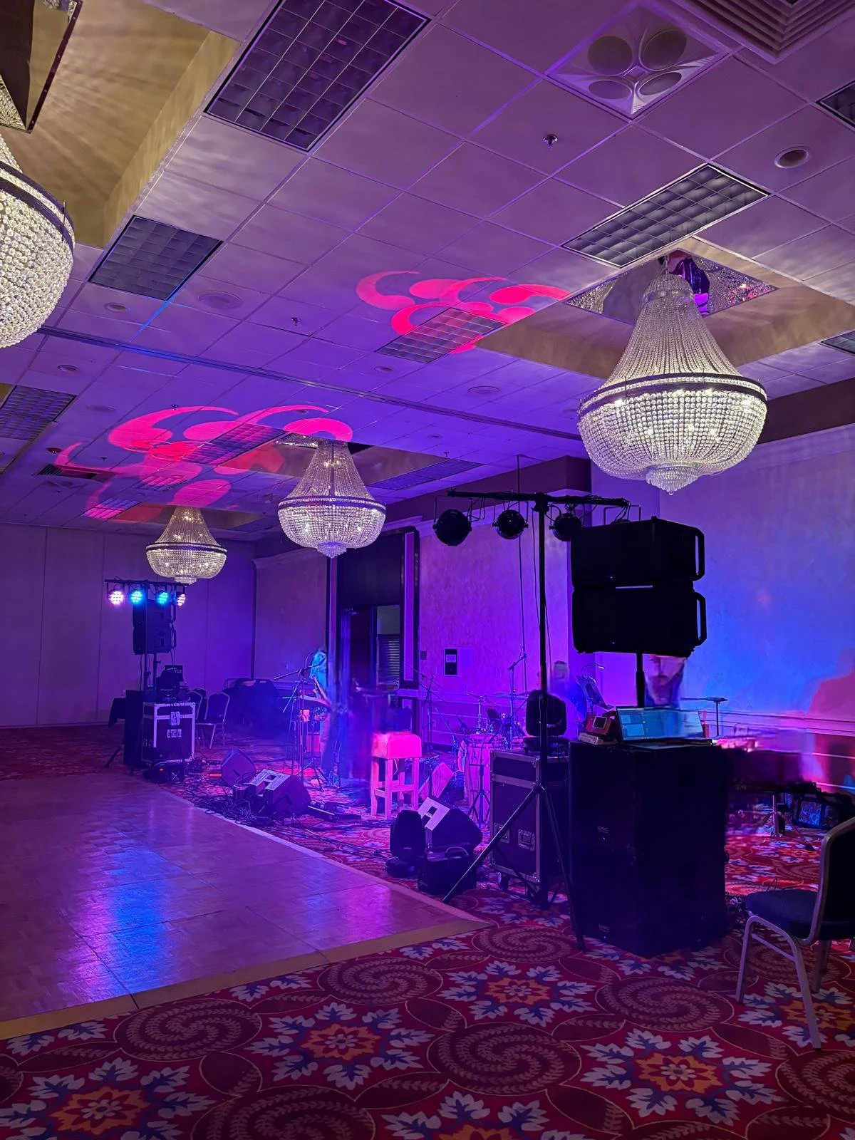Empty banquet hall with chandeliers, stage lighting, and musical equipment, set for an event or performance.