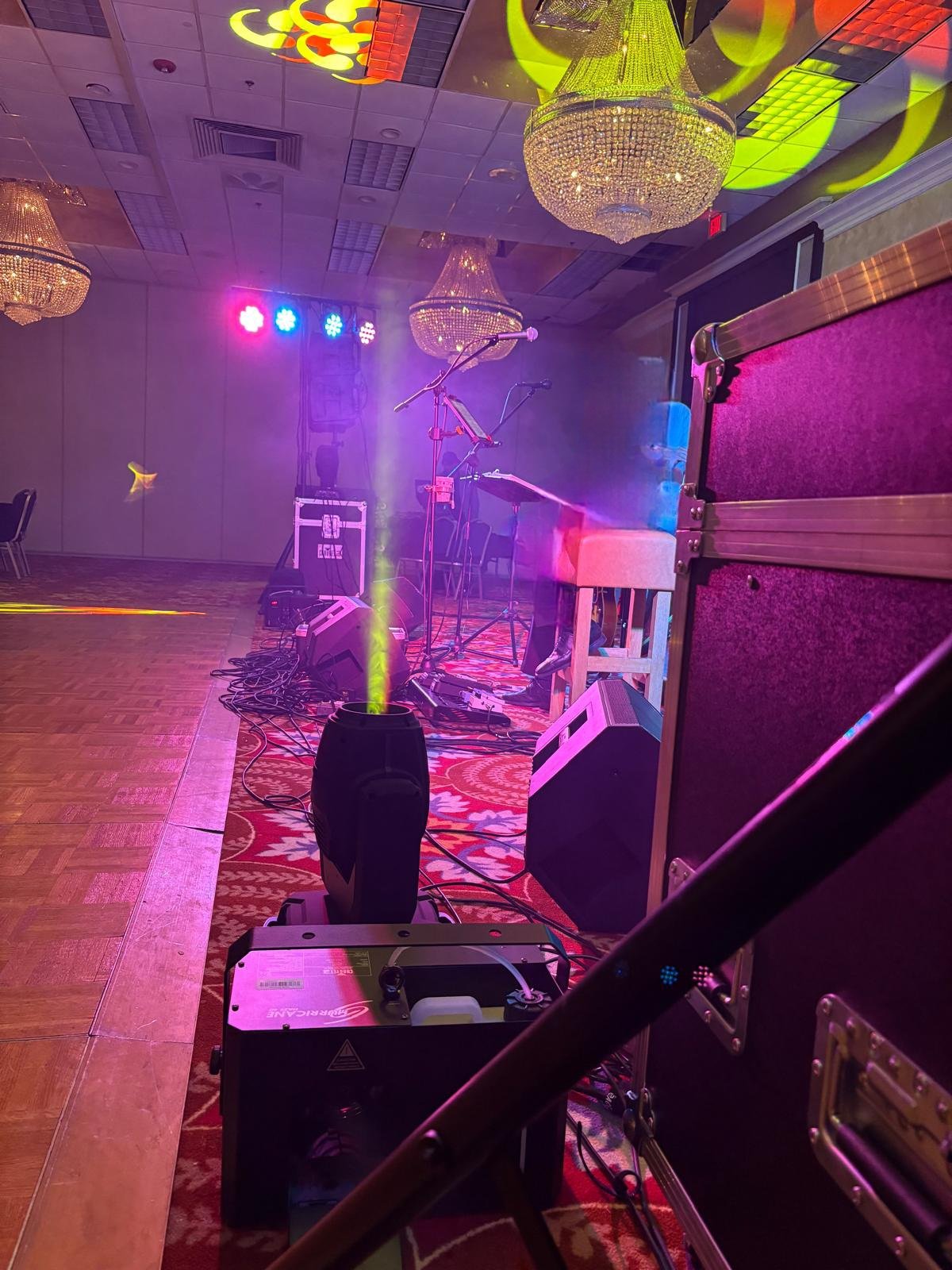 Stage set up with musical equipment, microphones, speakers, colorful lighting, and chandeliers in an event hall.