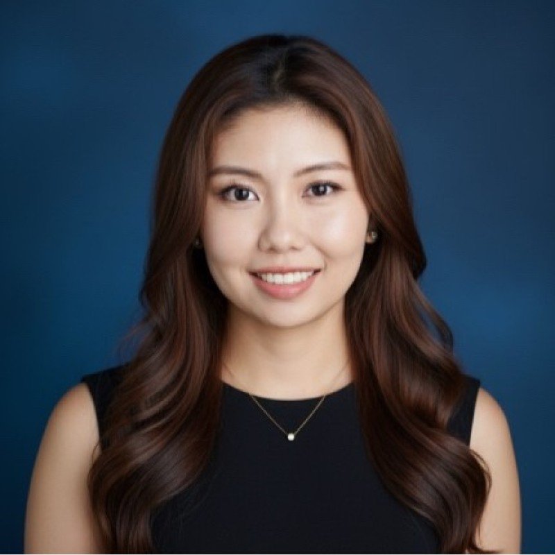 A portrait of a young woman with long wavy brown hair, wearing a black sleeveless top and a delicate necklace, smiling against a blue background.