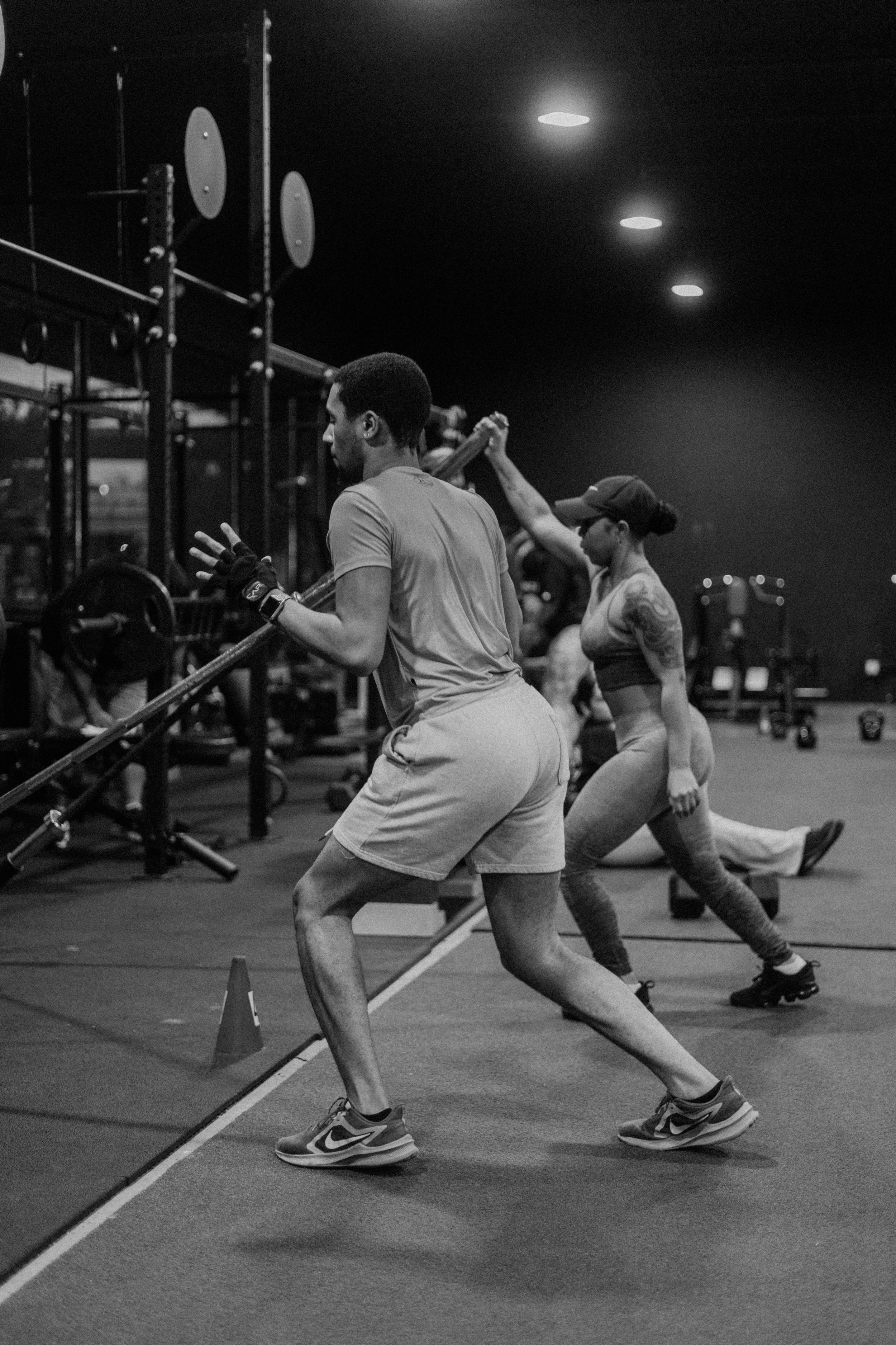 People working out with barbells and kettlebells in a gym, performing various strength exercises at night.