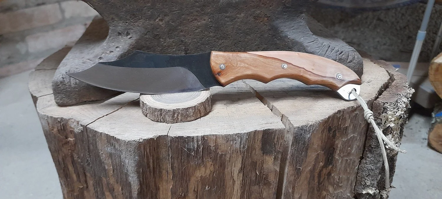 A hunting knife with a wooden handle and a black blade resting on a tree stump.