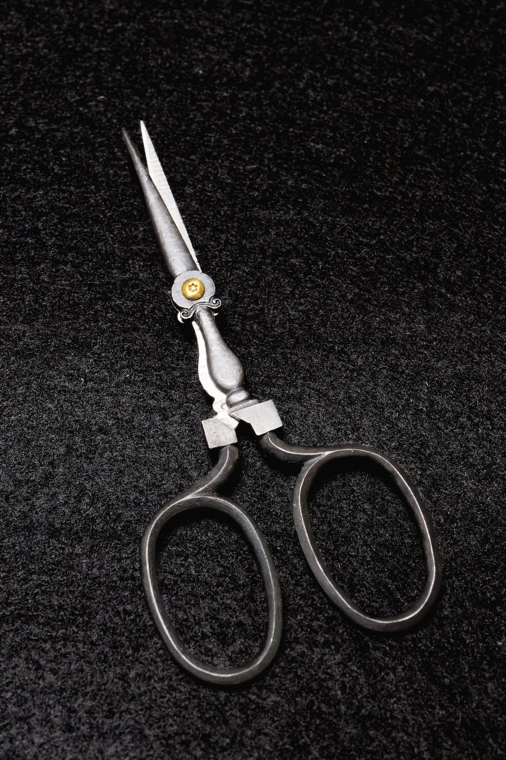 Close-up of vintage silver scissors with ornate handles on a black textured background.