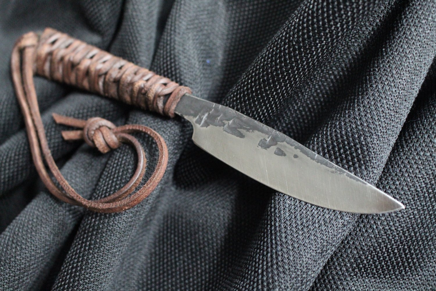 A small dagger with a curved, rusty handle and a dull, scratched metal blade, resting on a black textured fabric surface.