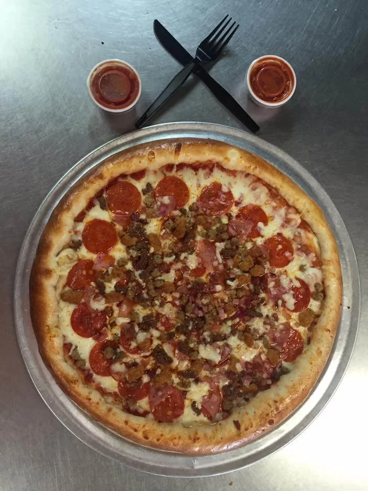 strombolis-starkville-pepperonisausagepizza.jpg → Pepperoni and sausage pizza on a metal pan with dipping sauce and utensils.