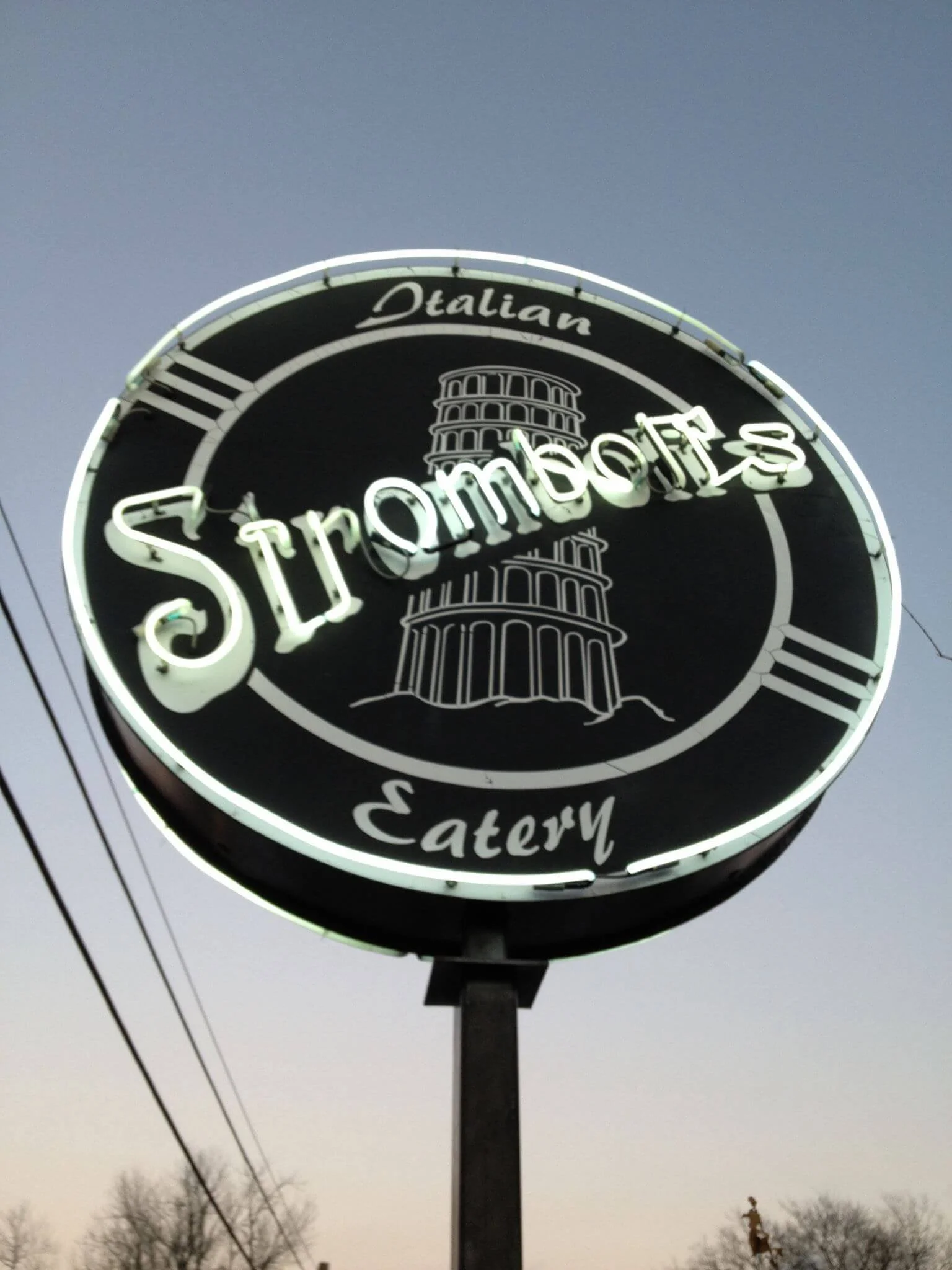 strombolis-starkville-neonsign.jpg → Neon Stromboli’s Italian Eatery sign glowing at dusk with the Leaning Tower of Pisa design.