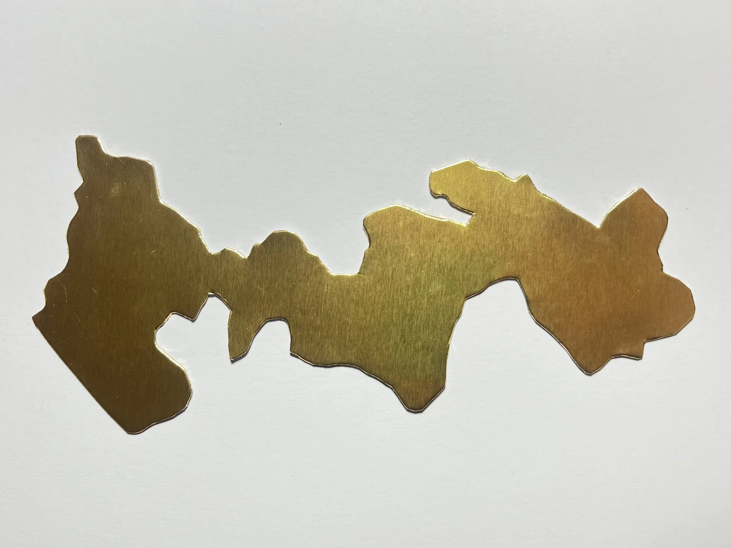 A metallic gold-colored cutout in an organic irregularly shape placed on a white background.