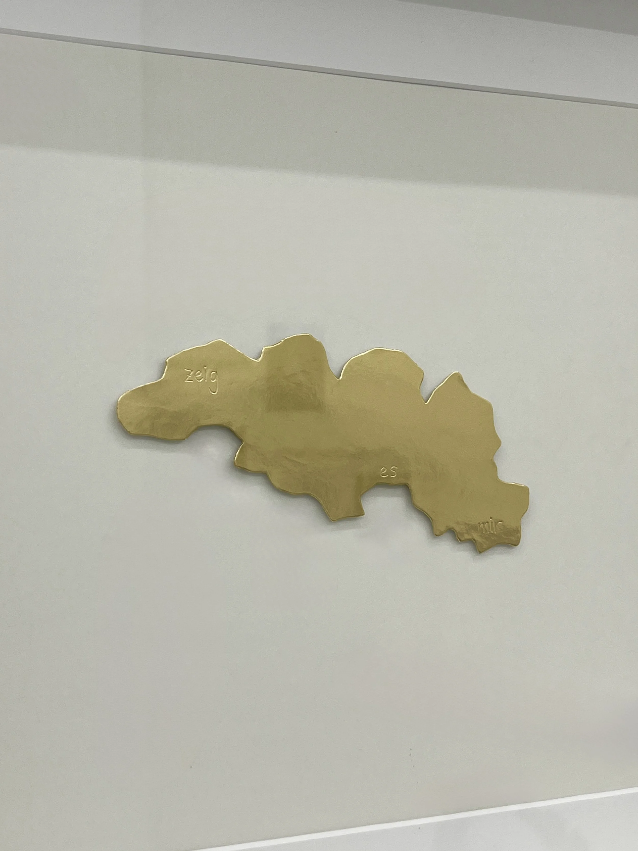 A metallic gold-colored cutout in an organic irregularly shape placed on a white background.