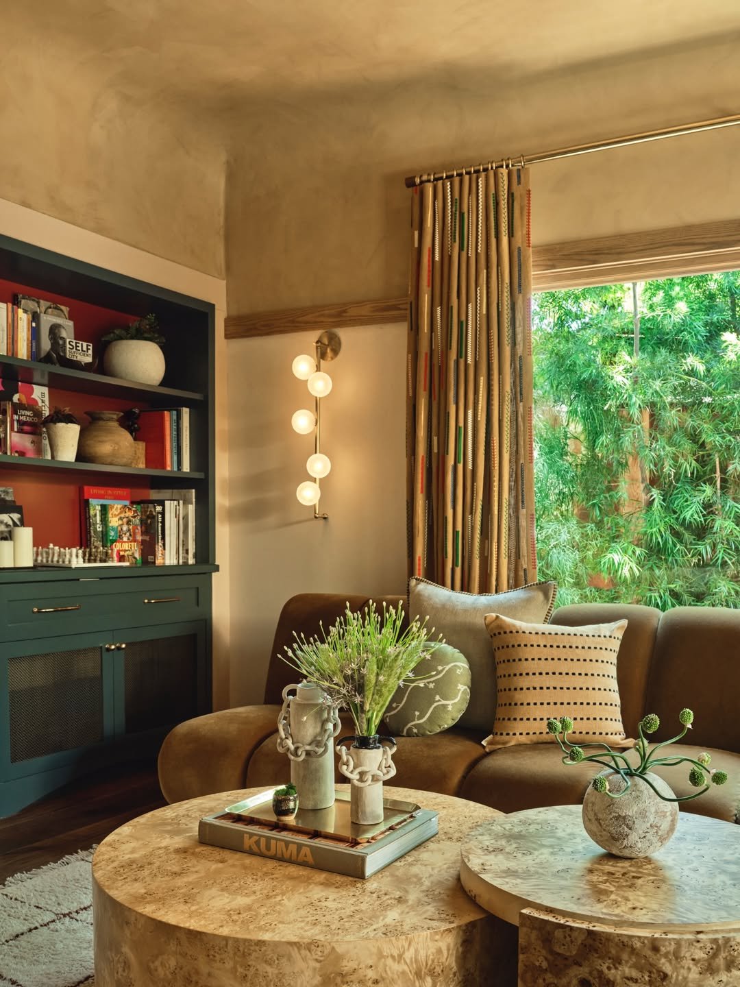Small space luxury living room with custom green built-ins, burl wood tables, textured pillows, and natural light.
