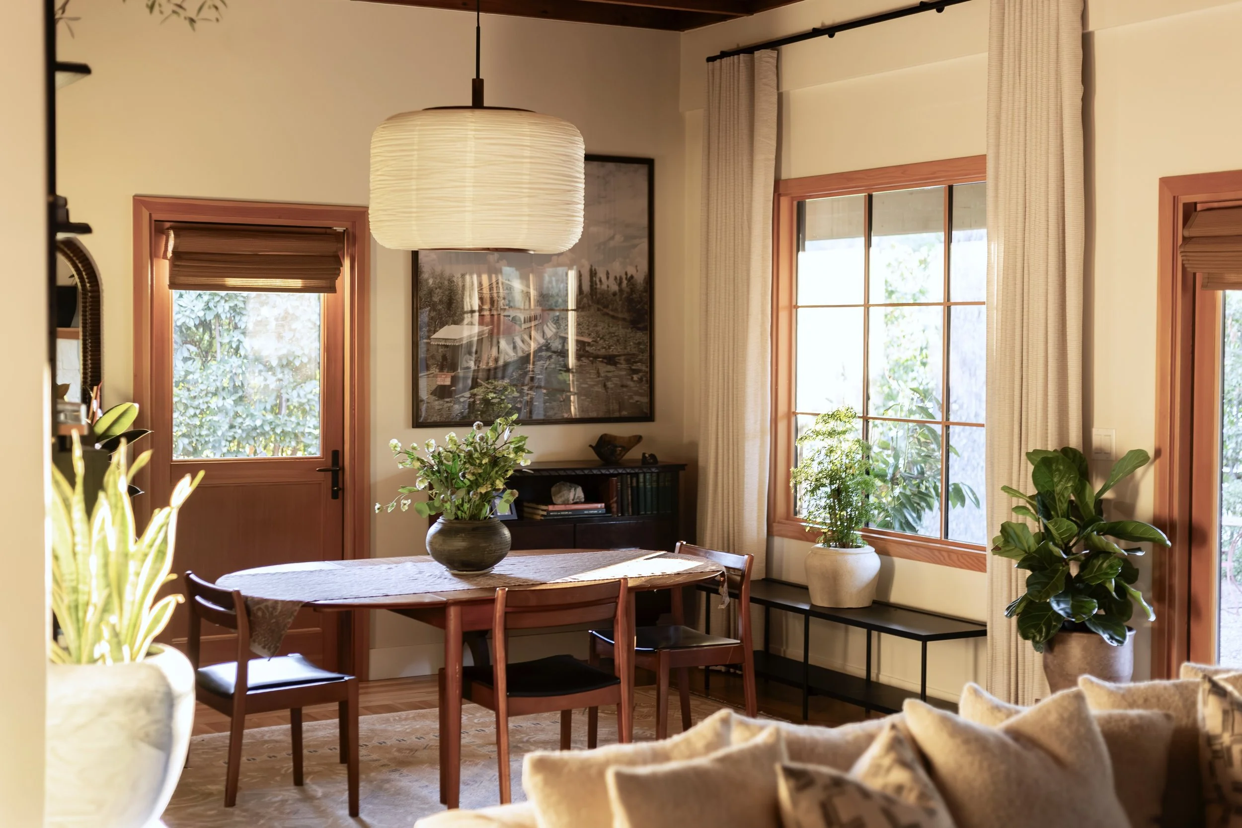 Small space luxury dining room with round wood table, neutral plaster walls, linen drapery, and soft natural light.