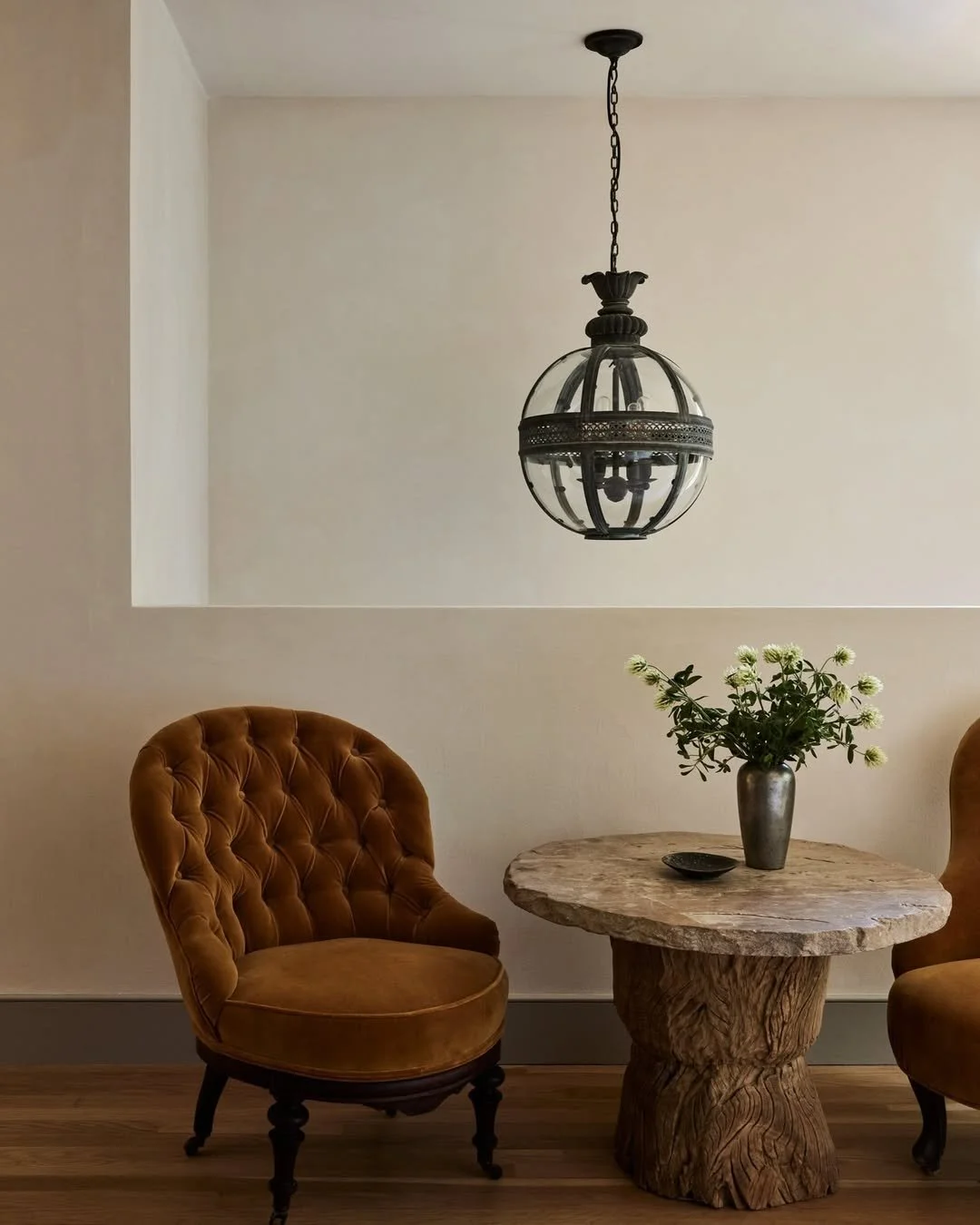 Luxury seating nook with tufted velvet chairs, sculptural stone pedestal table, and vintage glass pendant lighting.