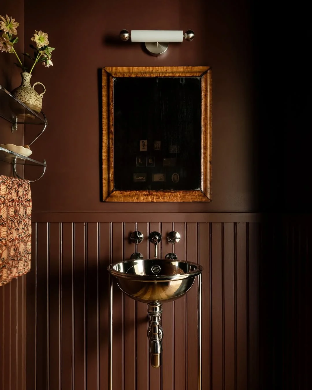 Moody brown powder room with brass pedestal sink and beadboard paneling creating a warm, intimate luxury interior.