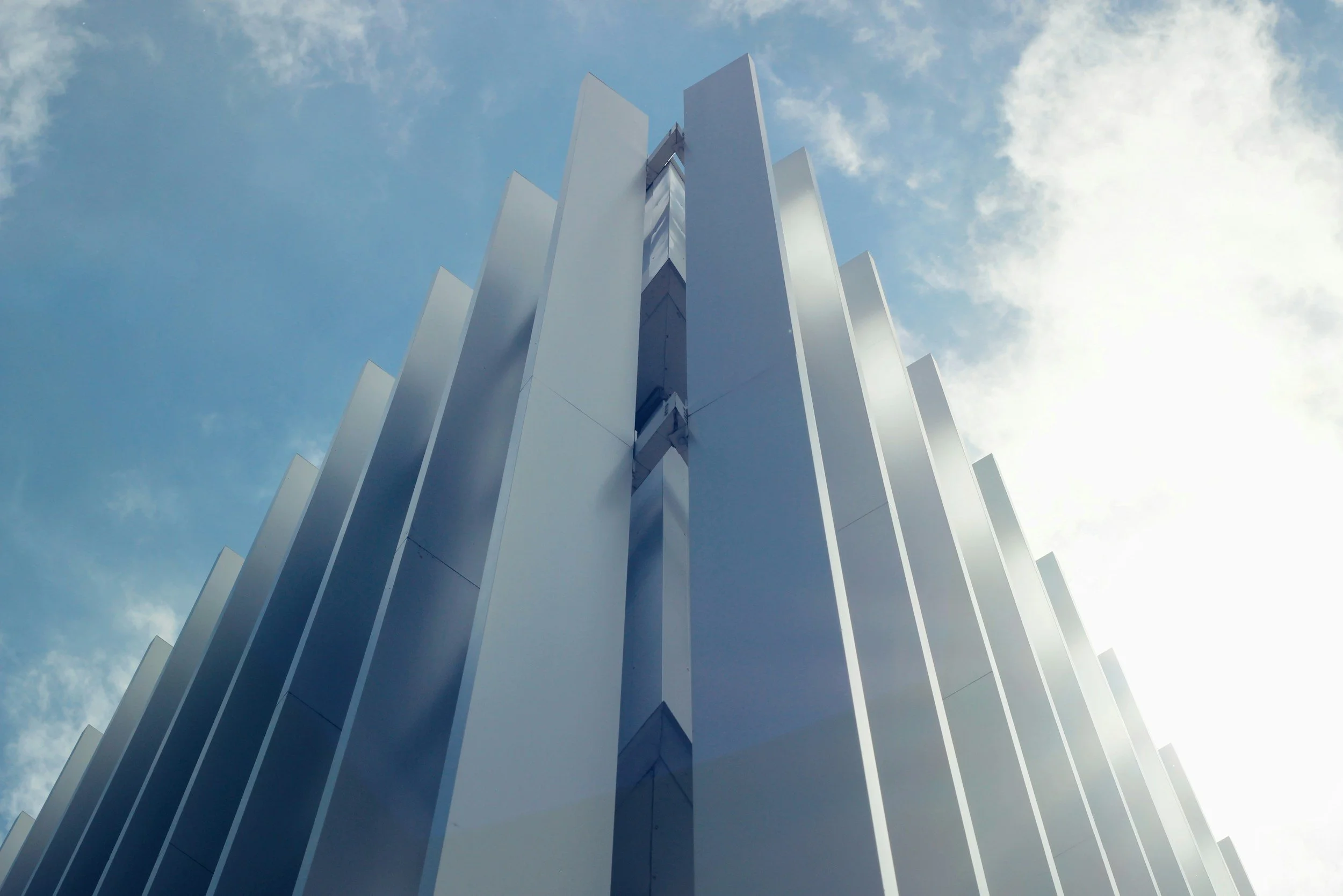 Low angle view of a modern high-rise building with vertical white panels under a partly cloudy sky.
