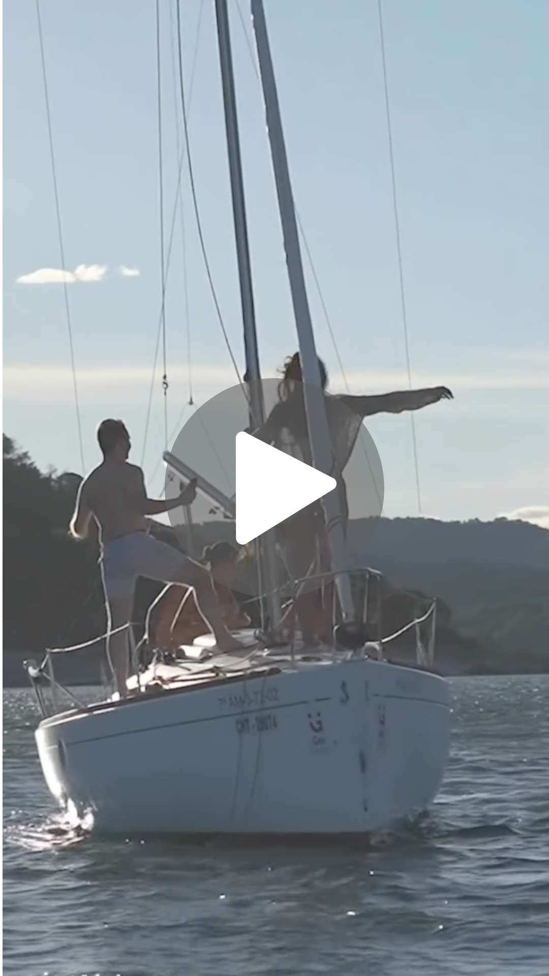 Personas navegando en un velero en el agua durante un día soleado, con un fondo de colinas y cielo despejado.