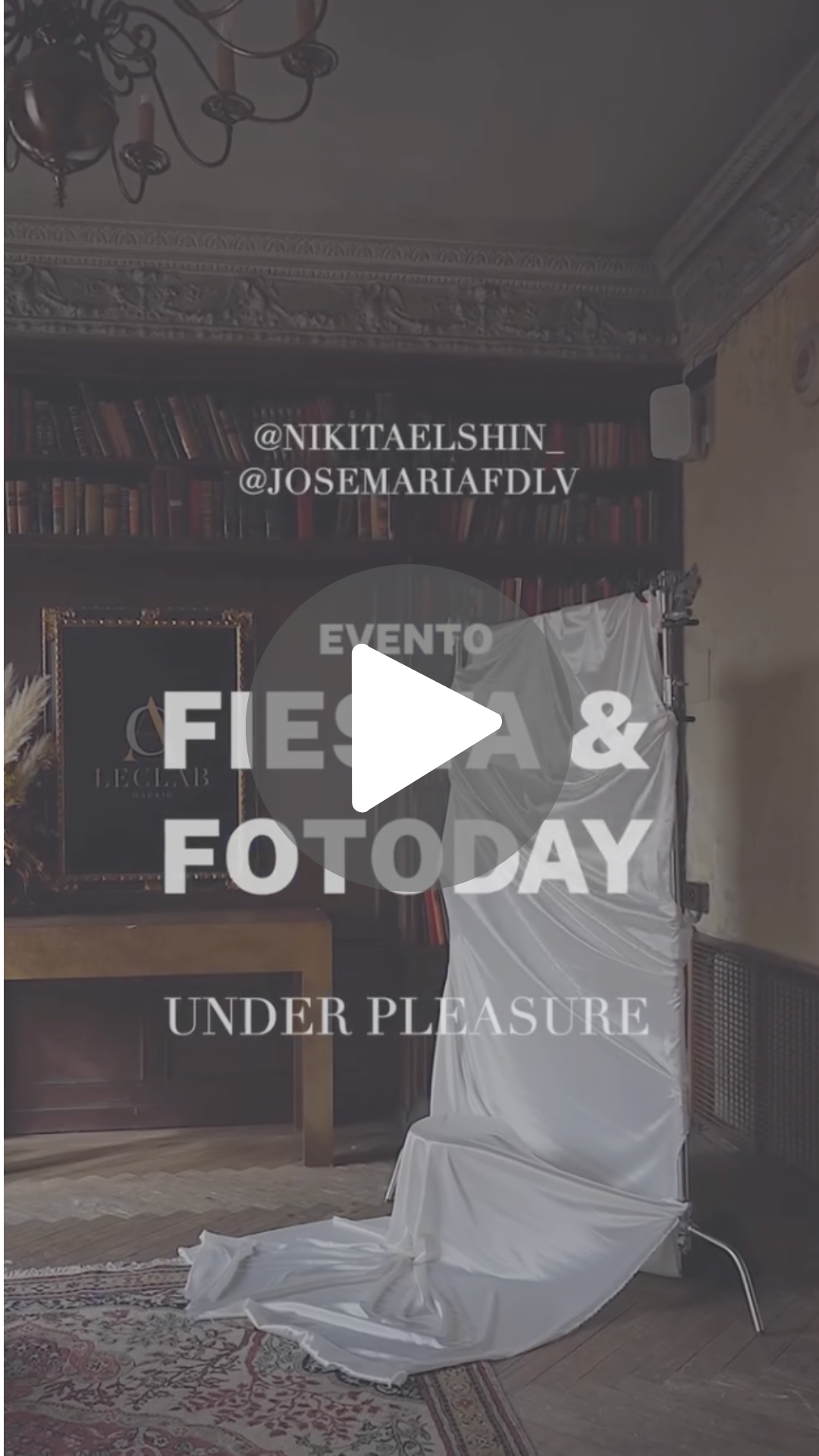 Texto en pantalla que promociona un evento llamado 'Fiesa & Fotoday' con la frase 'Under Pleasure', en un fondo de una sala con estanterías llenas de libros y un soporte de fotografía cubierto con tela blanca, en un ambiente elegante con un candelabro en el techo.