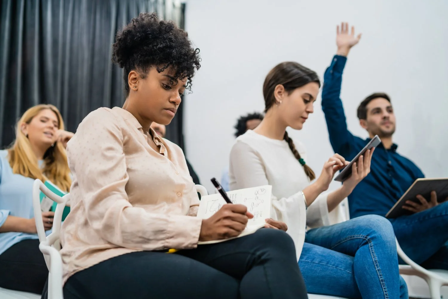 Group of diverse professionals attending a conference or seminar, seated in chairs, smiling, and engaged. Photo: Mego Studio