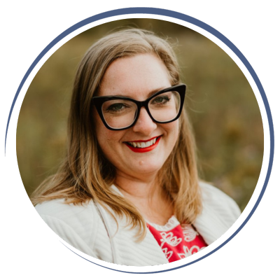 A woman with long blonde hair, black glasses, and red lipstick smiling outdoors.