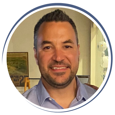 Headshot of a smiling man with short dark hair, beard, wearing a light blue collared shirt.