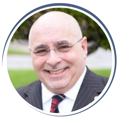 Smiling bald man wearing glasses and a suit outdoors.