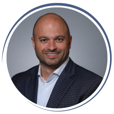 Close-up portrait of a smiling man with a bald head and a short beard, wearing a checkered blazer and white shirt, against a gray background.