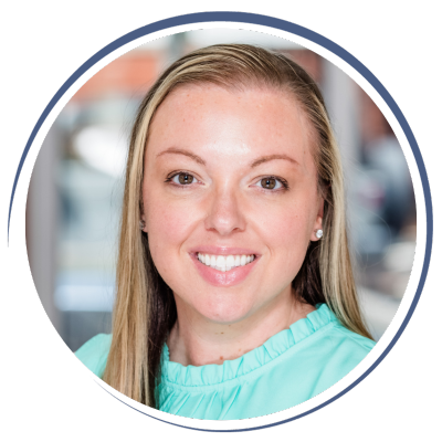A smiling woman with long blonde hair, wearing a light turquoise top, in an indoor setting.