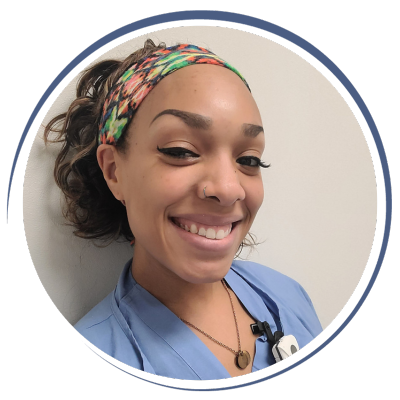 Young woman with curly hair, wearing a colorful headband and blue scrubs, smiling.