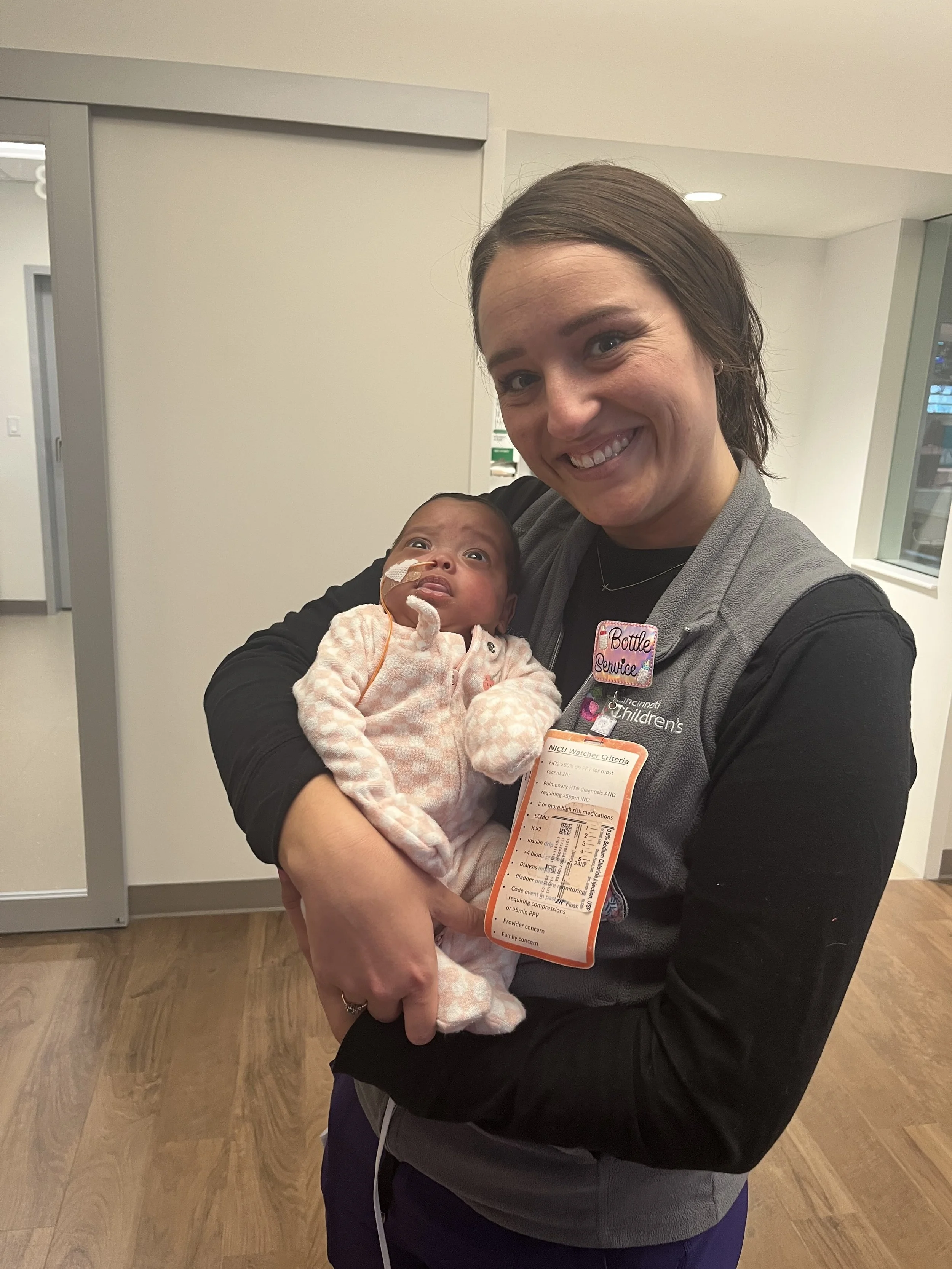 A woman holding a premature baby at a hospital. The woman is smiling, and the baby has a breathing tube and is wrapped in a blanket.