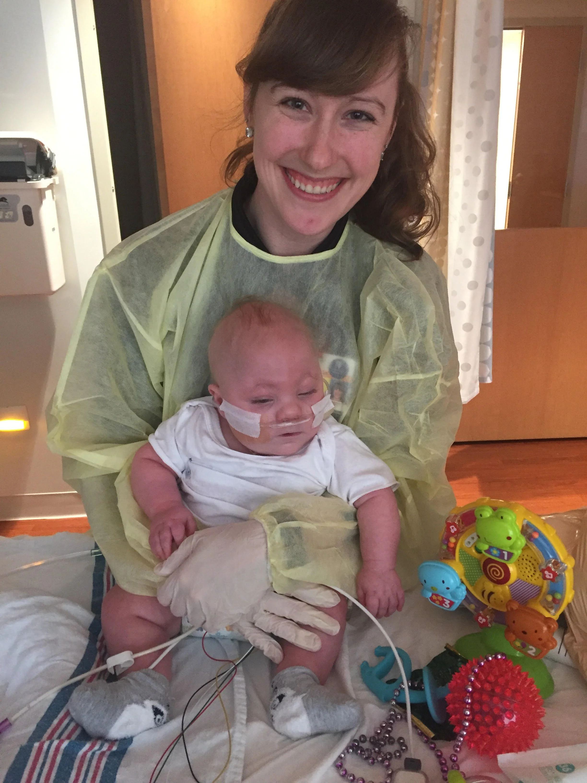 A woman in a hospital gown holding a young child with medical tubes and bandages, smiling.