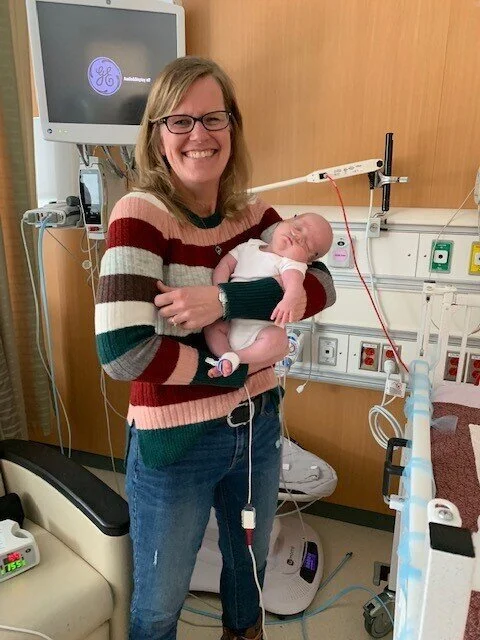 A woman holding a baby in a hospital room with medical equipment in the background.