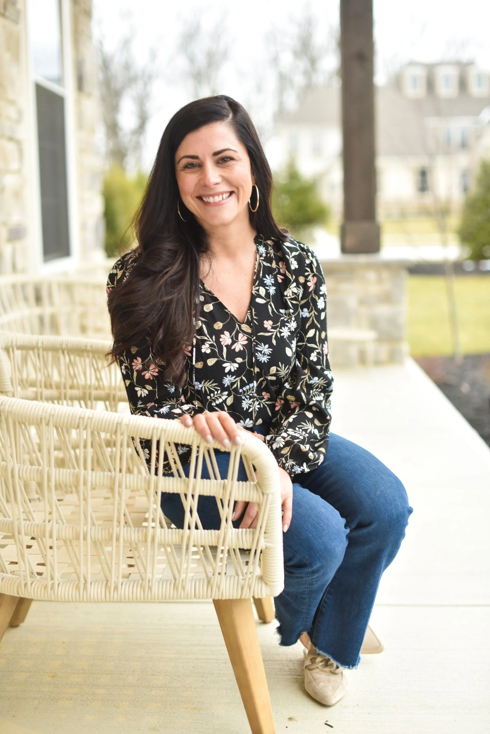 A woman with long dark hair smiling in front of a building, wearing a navy blazer and light scarf.