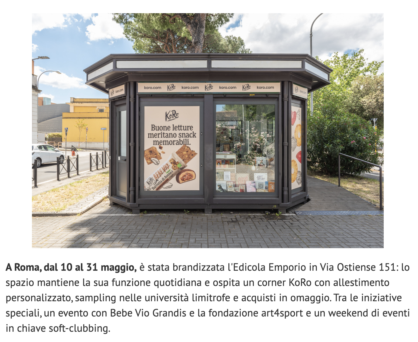 Koro, piccolo chiosco nero con grandi finestre di vetro, situato in strada con panchine, ai lati ci sono piante e alberi, il cielo è di giorno con nuvole sparse.