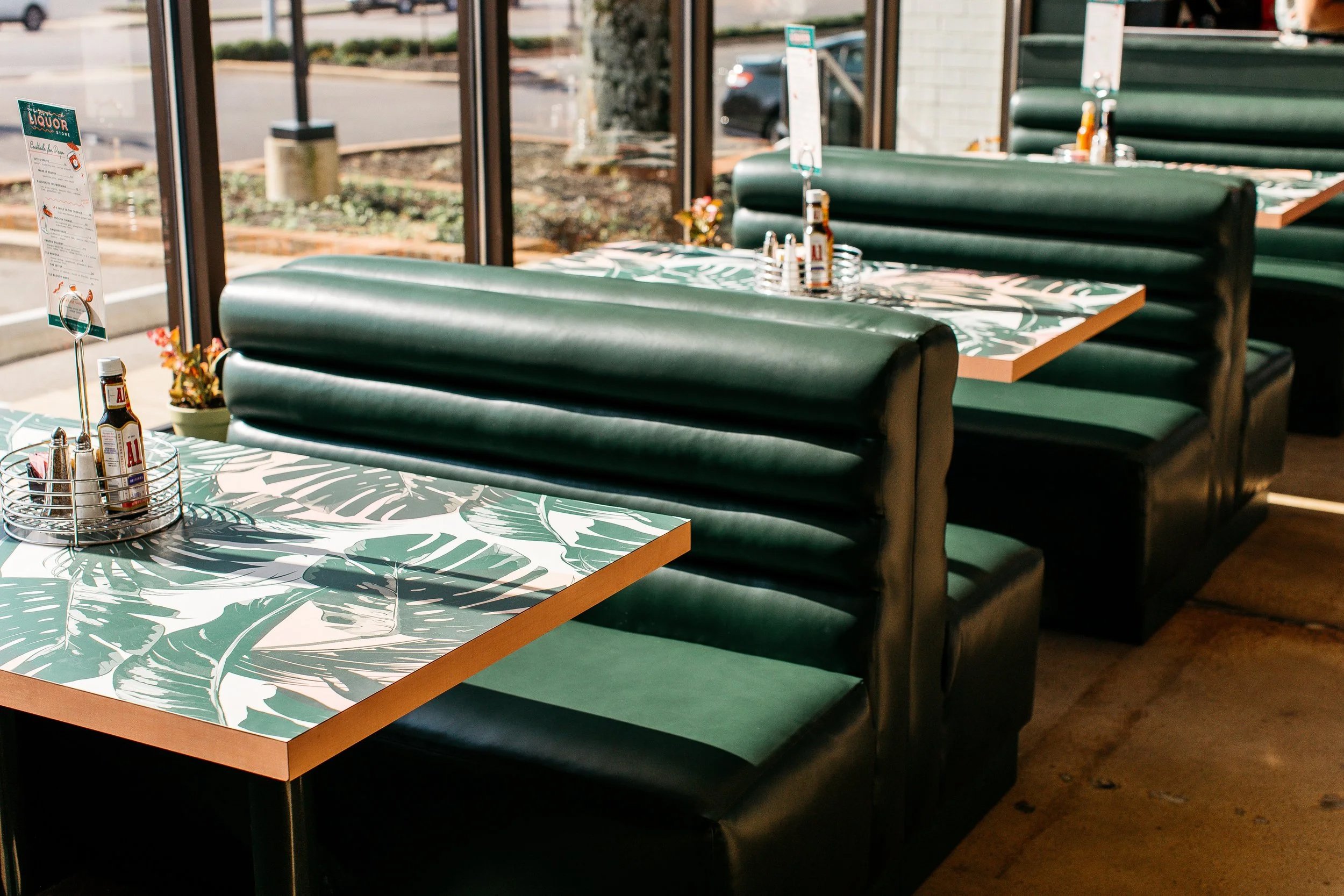 Empty booth seats with green backrests and tropical leaf patterned tabletops inside a restaurant