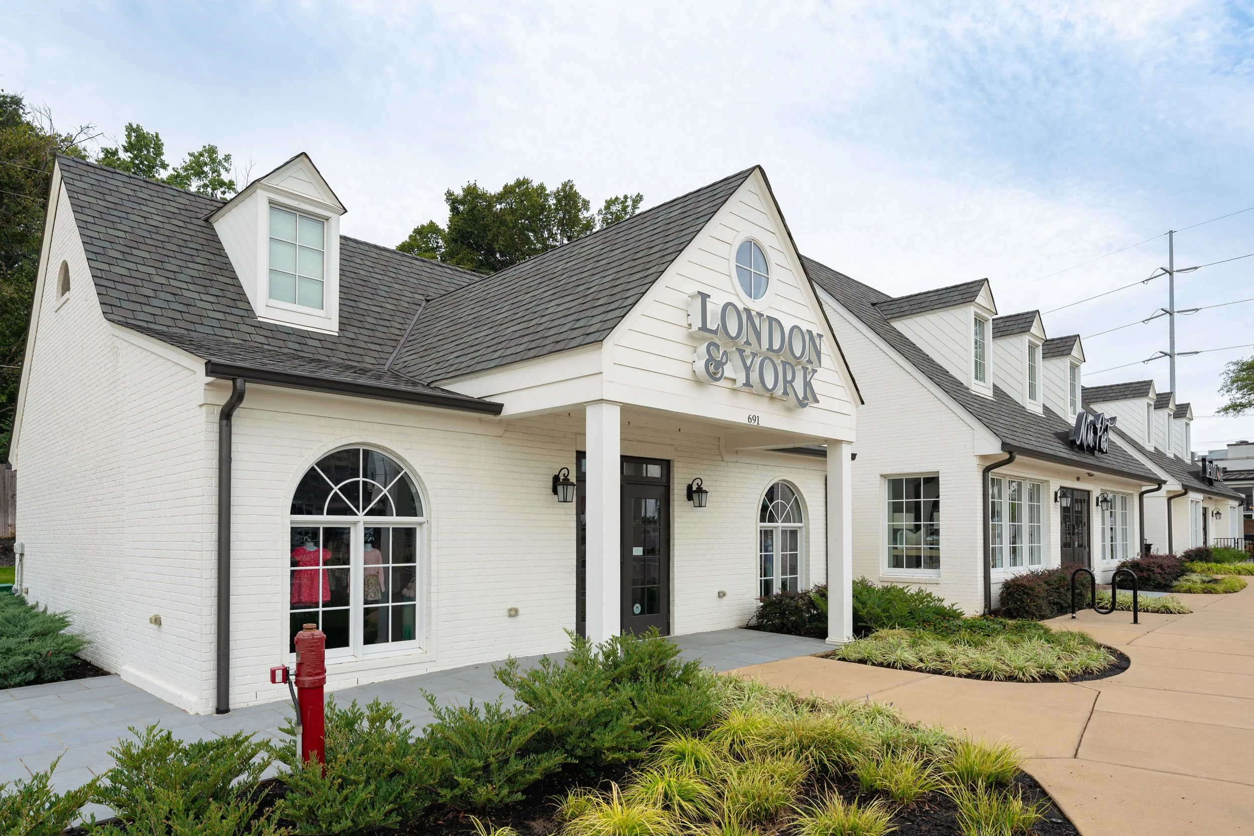 White building with a gabled roof, large windows, and the sign 'London & York' on the front. Landscaping with bushes and a sidewalk in front.
