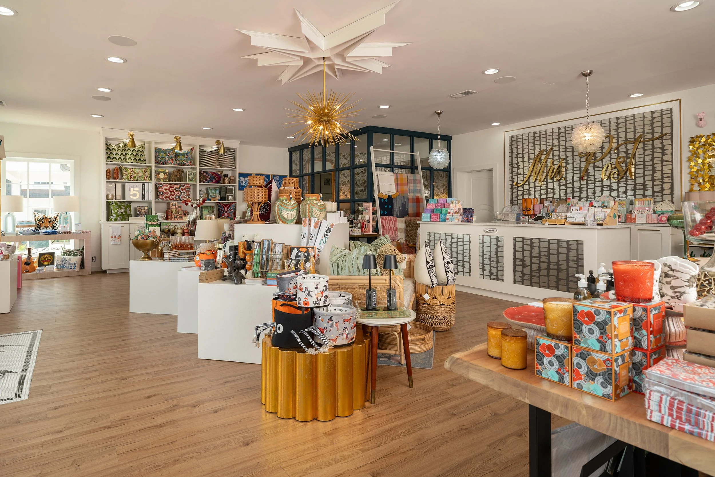Interior of a boutique store with shelves and tables displaying home decor, accessories, and gifts, with a decorated ceiling and a counter on the right.