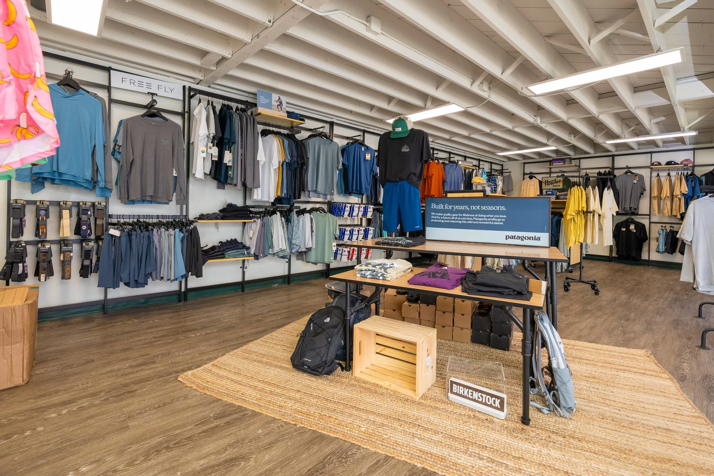 Interior of an outdoor clothing store with Patagonia apparel, hats, and accessories on display, and a wooden floor with a woven rug.