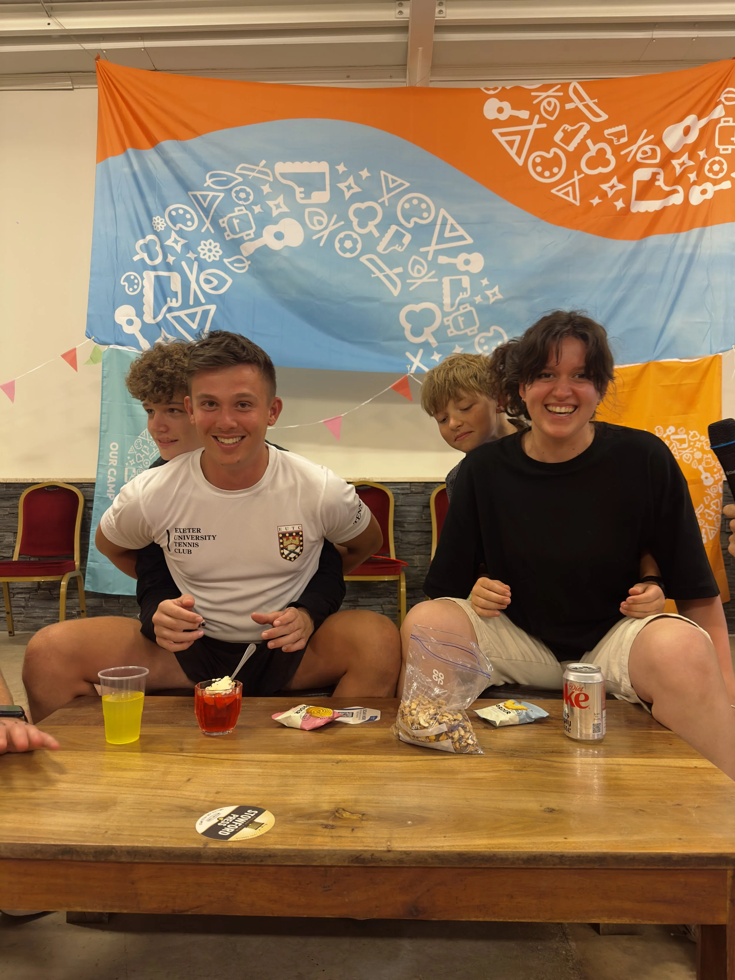 camper smiling in front of a large screen with the word 'OUR CAMP' illuminated, with colorful lighting. Practicing fluency and public speaking at Hereford UK - Our Camp English Language Summer Camp.