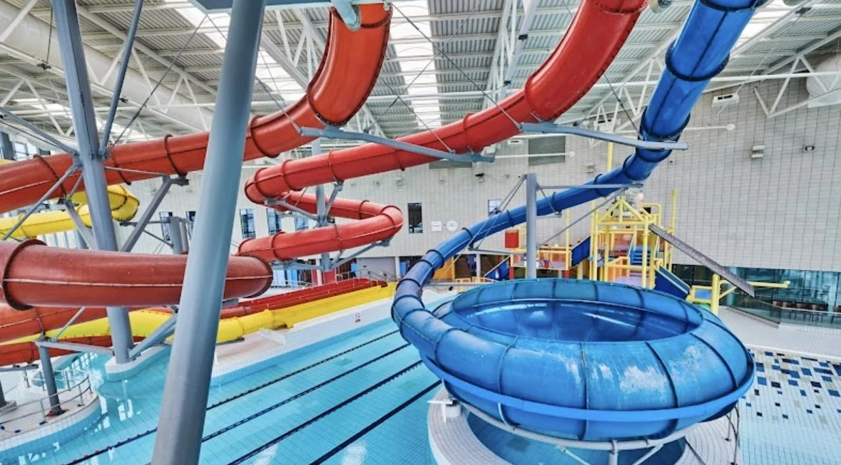 Group of five children and two adults in canoes on a river, surrounded by lush green trees, with some showing thumbs up and smiling. Adventure activities at Hereford UK - Our Camp English Language Summer Camp.