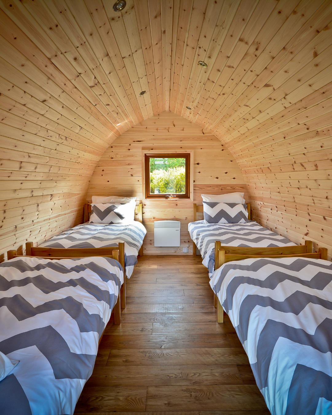 A wooden cabin with an arched roof on a grassy area surrounded by trees under a clear blue sky at Our Camp international summer camp UK in the beautiful Hereford countryside.