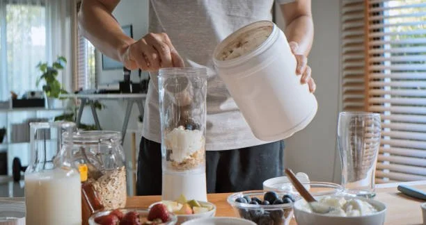 Person making a smoothie with a blender and various fruits and ingredients on the counter