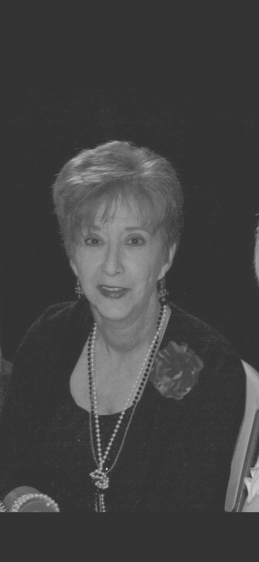 Black and white portrait of an older woman with short dark hair, wearing a textured top, looking directly at the camera.