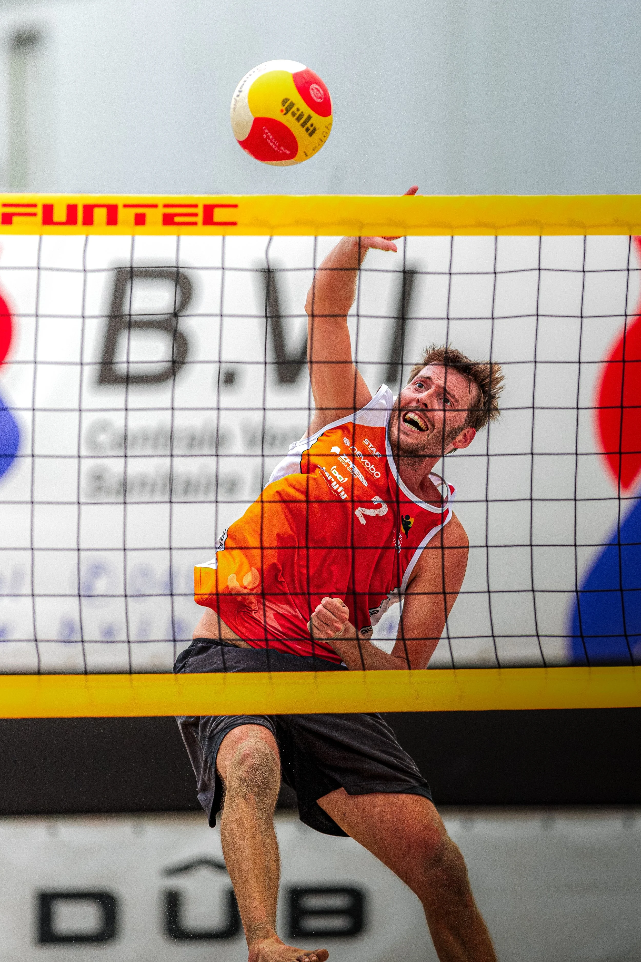 Een man speelt volleybal tijdens een wedstrijd, hij springt omhoog en probeert de bal over het net te slaan.