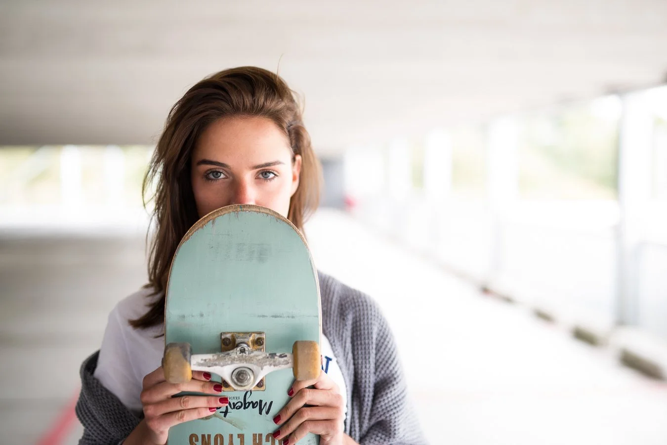 Vrouw houdt skateboard voor haar gezicht in een ondergrondse parkeerplaats.