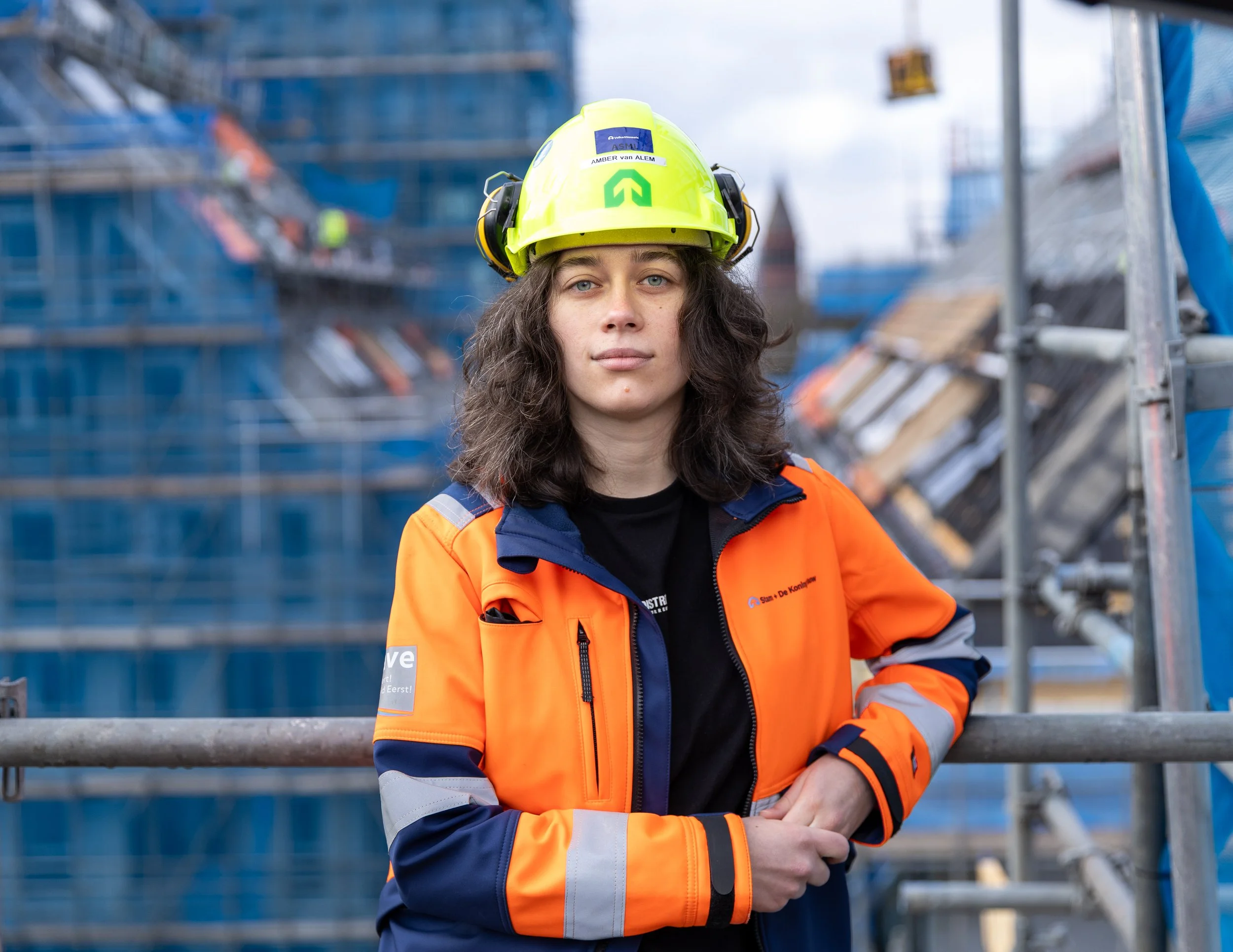 Vrouw in bouwoutfit en helm op een bouwplaats.