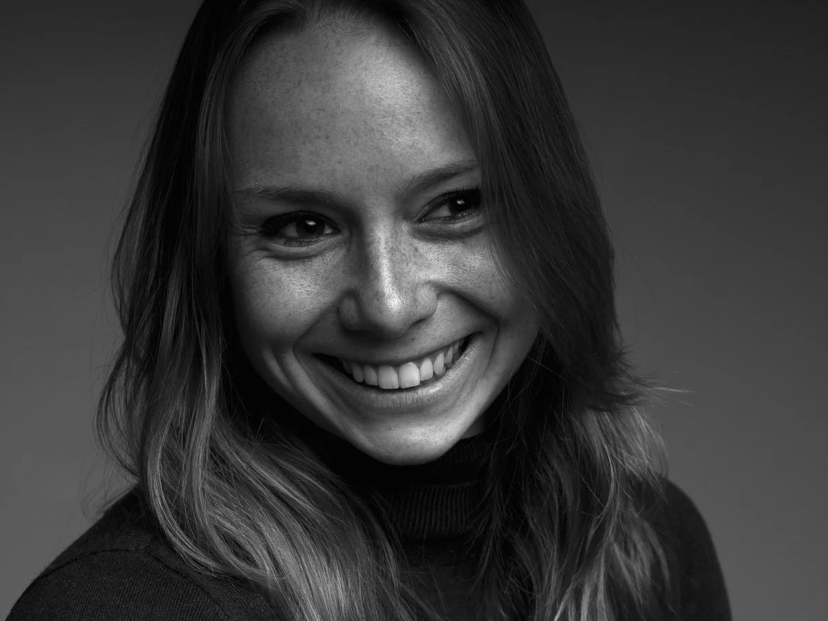 Zwarte en witte portretfoto van glimlachende vrouw met lang haar, doorstaand tussen de schouders, met een vlotte en ontspannen uitstraling.