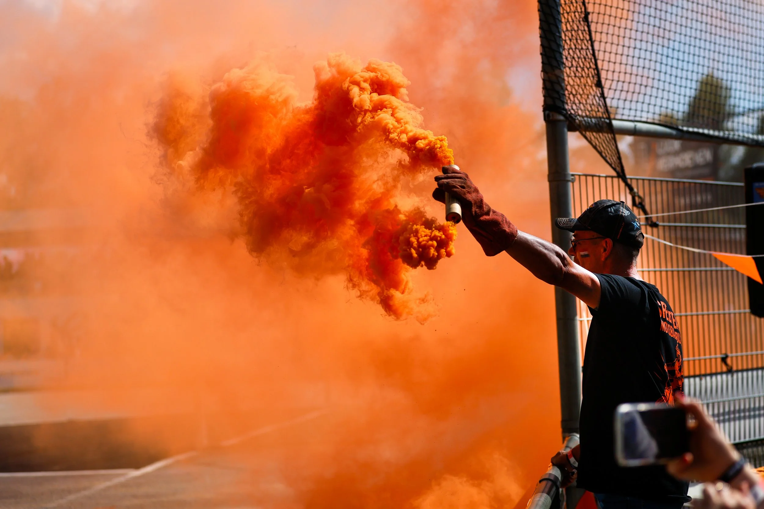 Man houdt een kleurrijke rookpot vast tijdens het EK Motoball in Budel met veel oranje rook.